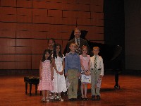 Teacher and 6 students stand by piano